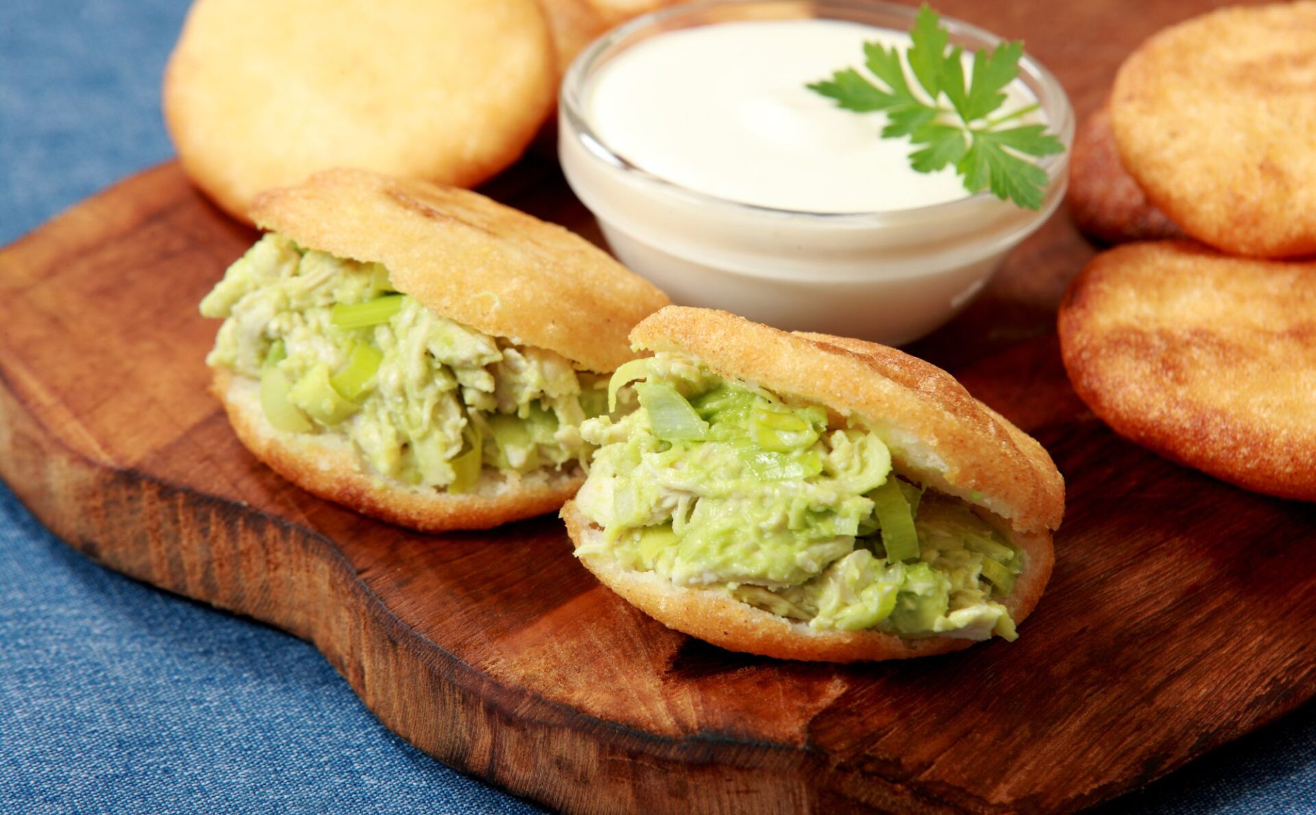 placuszki arepas, czyli dwa kukurydziane placki wypełnione nadzieniem z awokado, kurczaka i cebuli. Danie leży na drewnianej tacce w towarzystwie białego dipu i innych sosów.