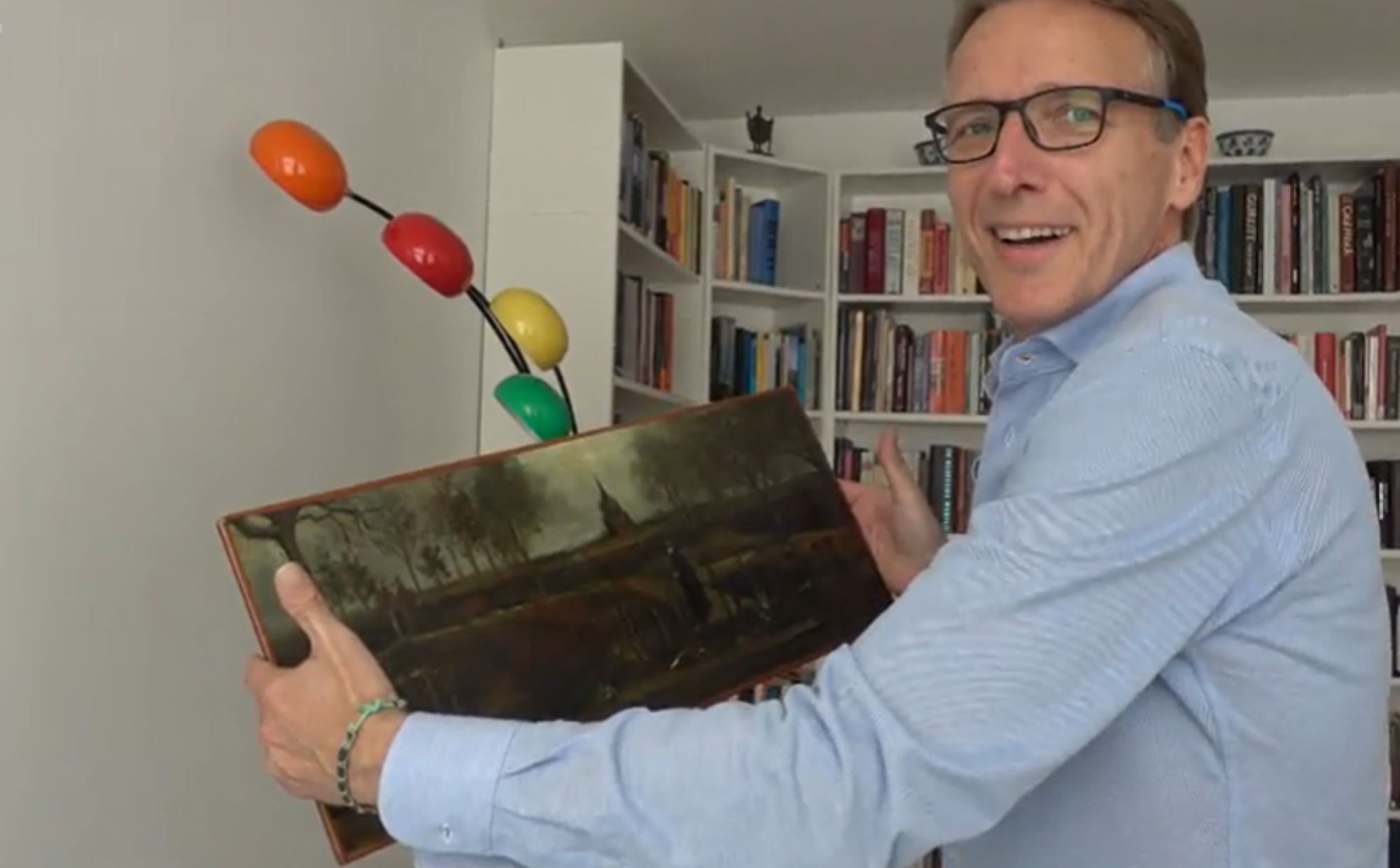 mężczyzna trzyma obraz, w tle półka z książkami,