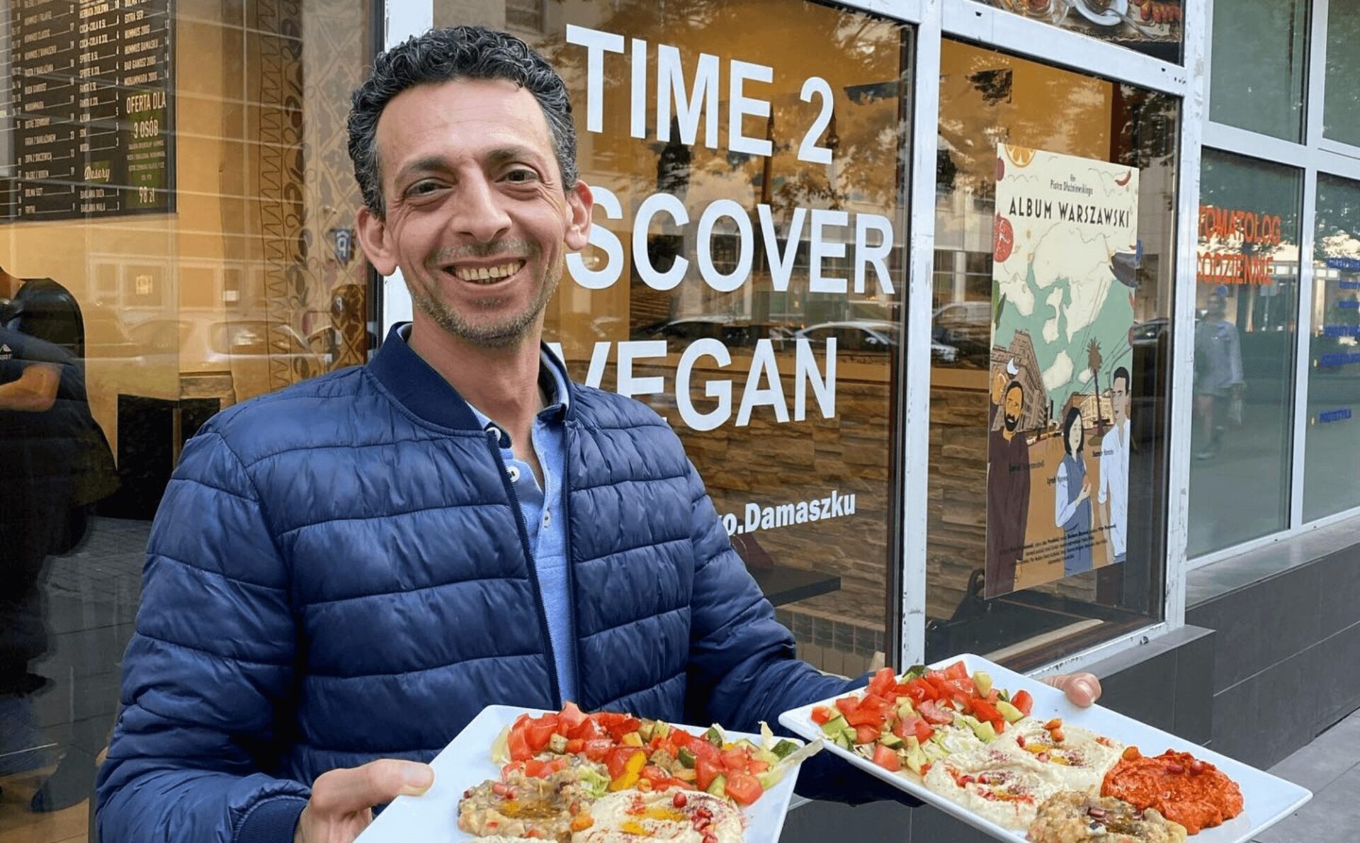 mężczyzna na zewnątrz restauracji prezentuje dania, trzyma talerze, na talerzach hummus, pasta z bakłażana, kuchnia syryjska, Niedaleko Damaszku