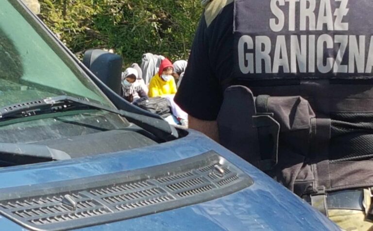 samochód, plecy funkcjonariusza straży granicznej i dzieci w maseczkach w tle