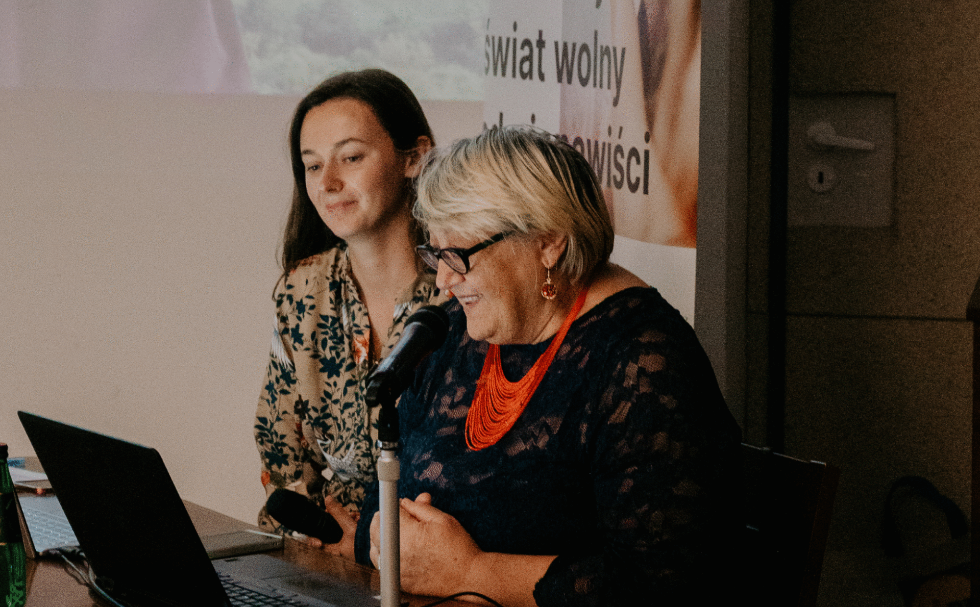 dwie kobiety siedzące przy stole ozdobionym gruzińską flagą