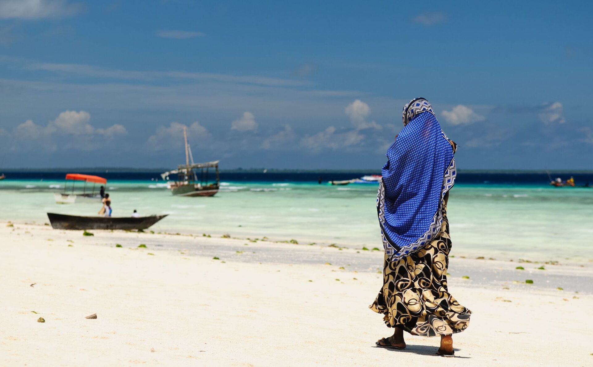 kobieta w kolorowym hidżabie przechadza się po plaży nad morzem