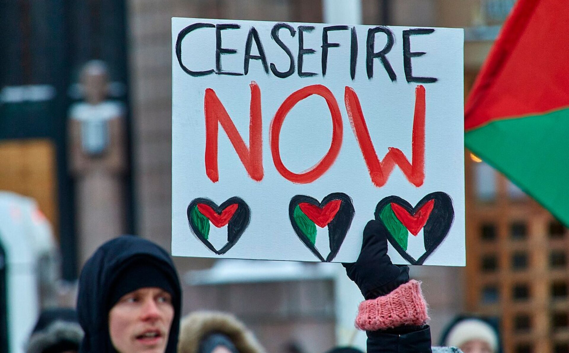 plakat ceasfire now trzymany przez młodego meżczyznę w kurtce