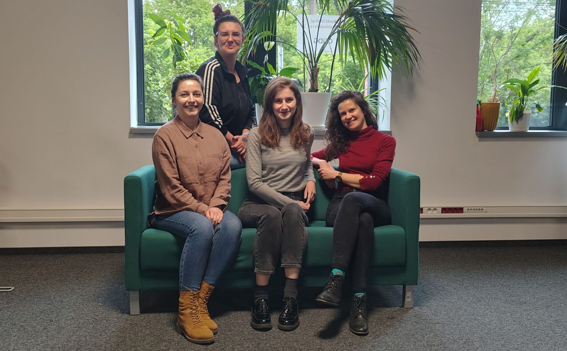 cztery kobiety na zielonej sofie w otoczeniu kwiatów doniczkowych